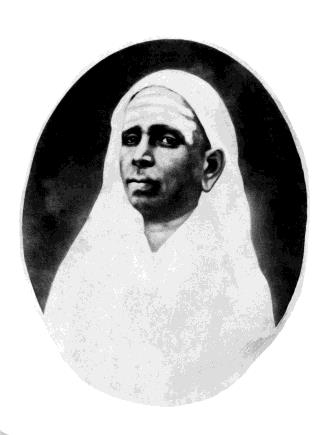 Oval-vignetted black-and-white portrait of an elderly woman with her head covered by a white cloth.