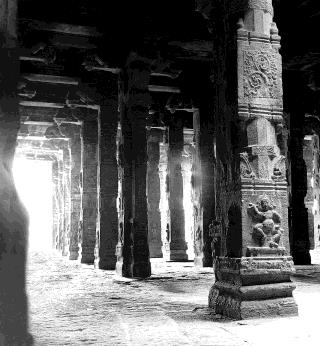Long colonnade of carved stone pillars in a temple hall, with bright light at the far end.