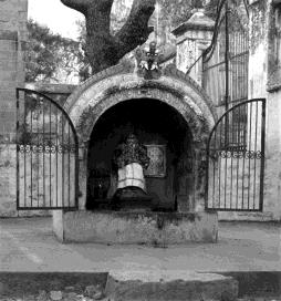 A small arched shrine with open iron gates, a tree behind.