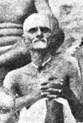 Grainy portrait of Palaniswami, an elderly bearded man with hands clasped at his chest.