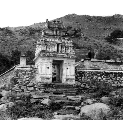 A small temple gateway tower with a stone wall and rough stone steps on a rocky hillside.