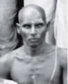 Close-up portrait of Gambhiram Seshayya, a shaven-headed bare-chested man.