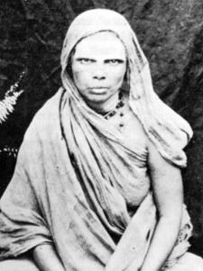 Black-and-white photograph of Echammal, an elderly woman seated, her head and shoulders covered with a draped cloth. Whole picture.
