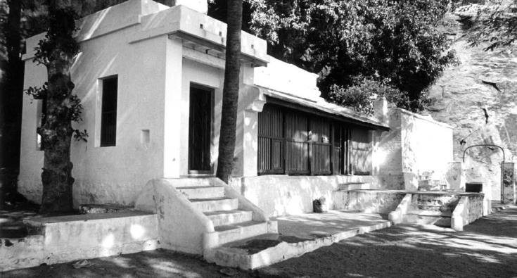 Black-and-white photograph of the front of Skandashram: a whitewashed building with steps, a verandah with barred windows, and a tree trunk in front. Whole picture.