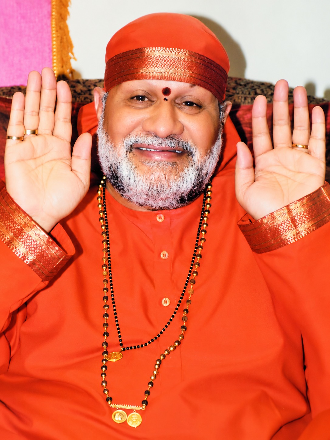 Sri Sai Das Babaji in saffron robes, smiling, both palms raised in blessing