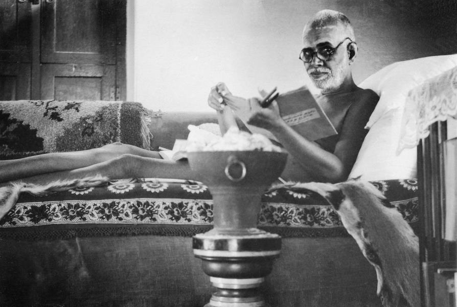 photograph: Sri Bhagavan reclining, wearing glasses, reading a book