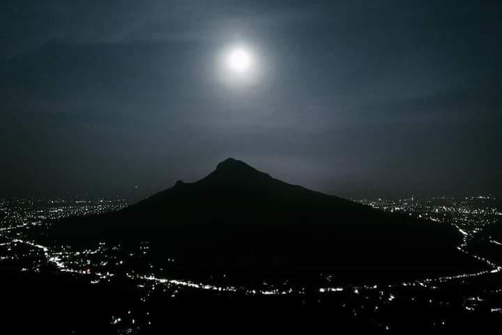 photo of Arunachala hill silhouetted at night under a bright moon, town lights below