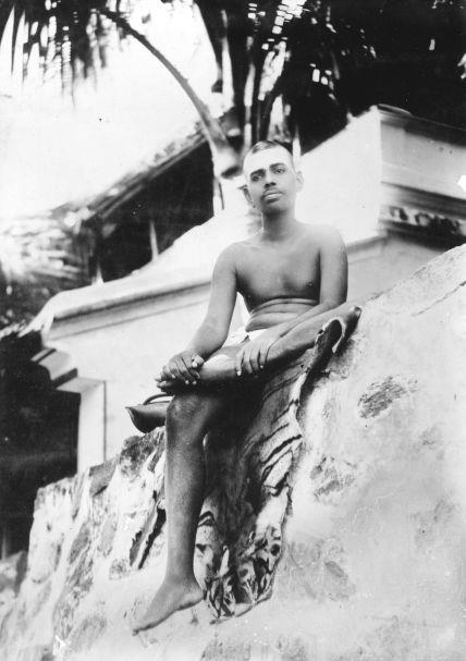 full-page photo of the young Sri Bhagavan seated on a rock outside Virupaksha Cave