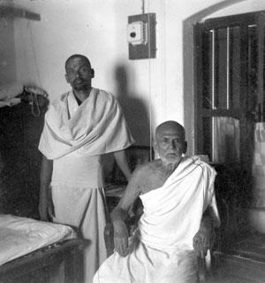 photo of Sadhu Om standing beside Sri Muruganar seated, in a room