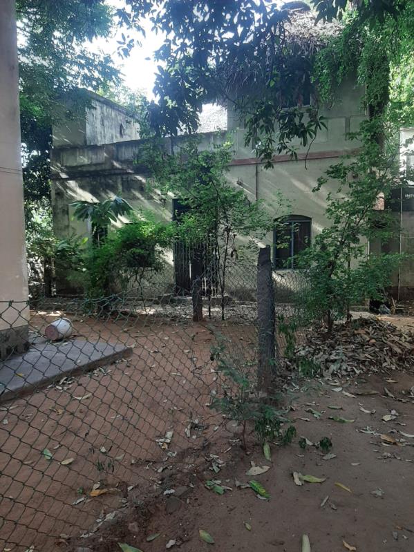 colour photo of a two-storey building behind trees and a wire-mesh fence (Dr. T.N.K Building)