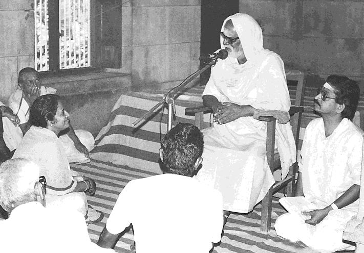 photo of Kunju Swami speaking into microphone with audience
