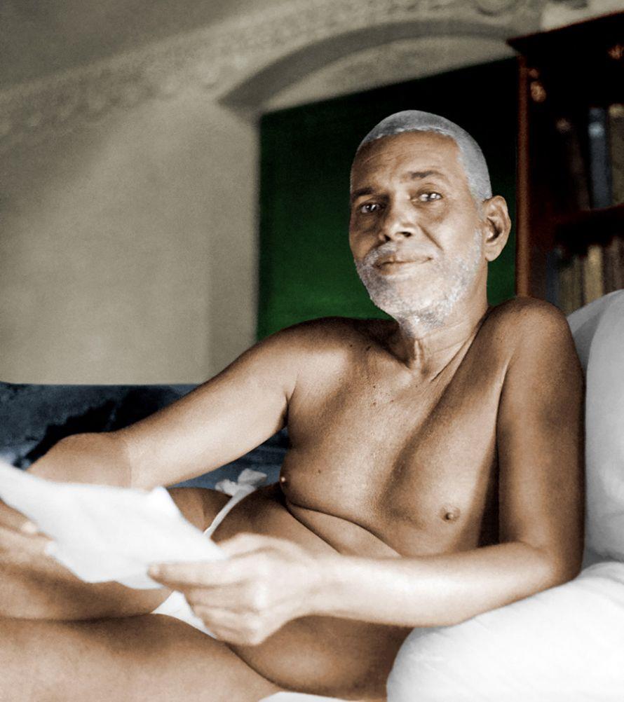 colour photo of Sri Bhagavan reclining on a couch holding papers