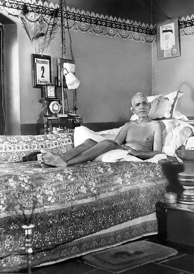 photograph of Sri Bhagavan reclining on a couch in the Old Hall, with a calendar (December 2, Tuesday), clock and lamp behind