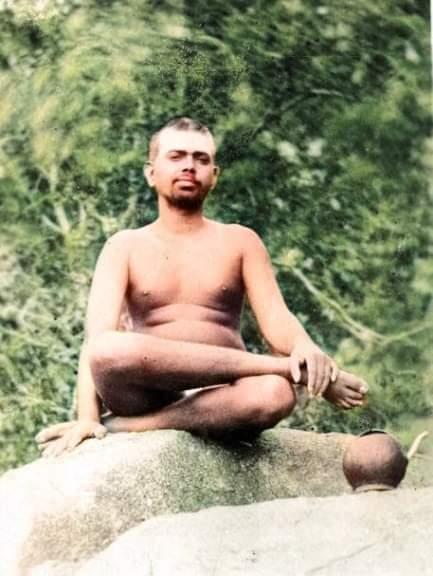 colour photo of a young man seated cross-legged on a rock, greenery behind, water pot beside (per caption, Sri Bhagavan at Virupaksha Cave)