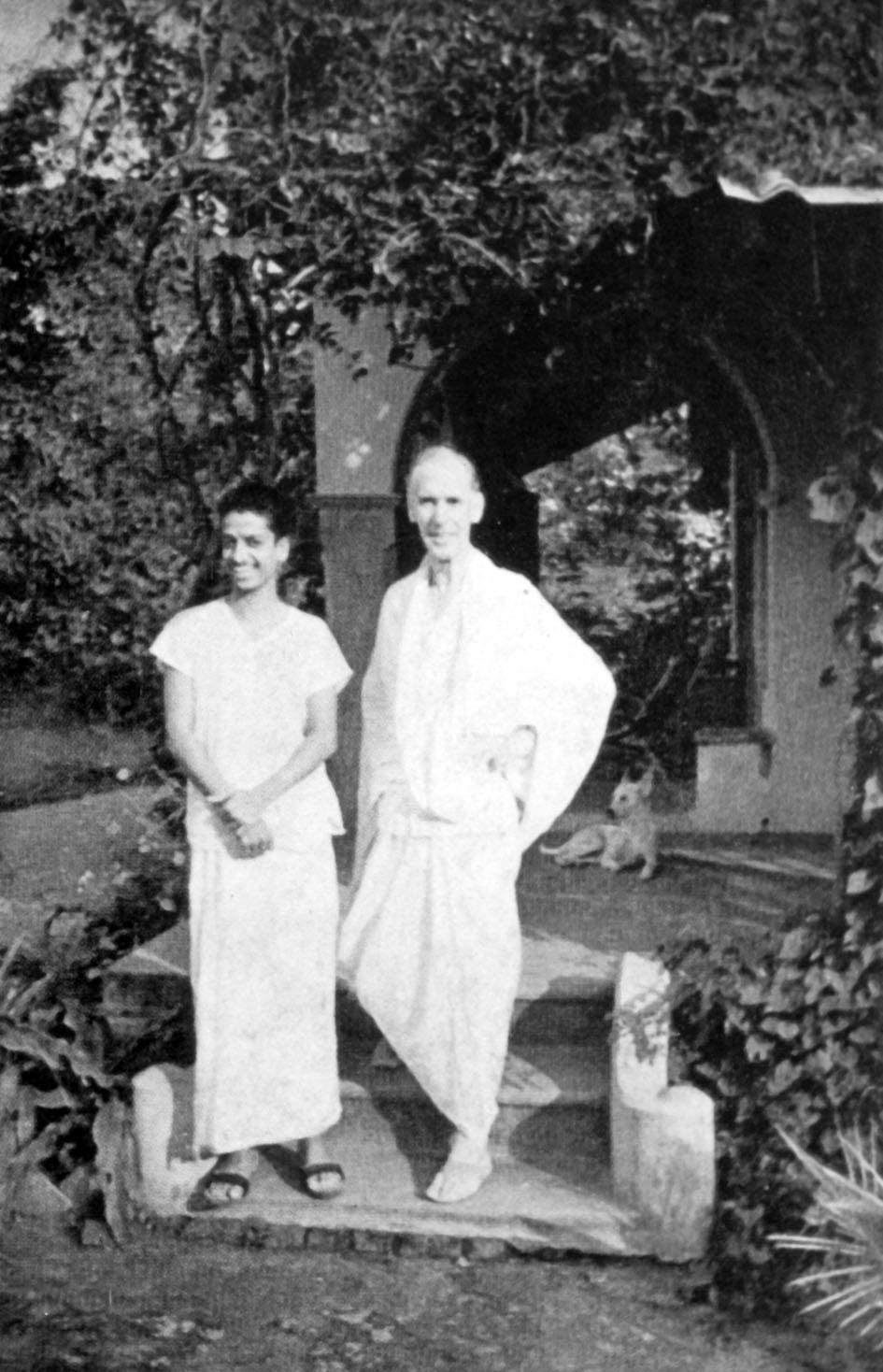 black-and-white photo of two men standing in a garden porch (V.Ganesan and Arthur Osborne per caption), dog behind