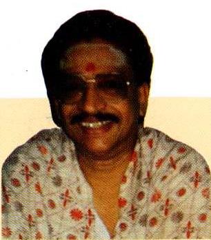 portrait photo of smiling man with red tilak in patterned shirt