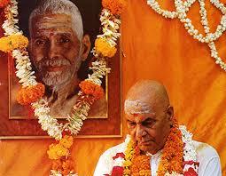 colour photo of Sri Papaji seated beside a garlanded portrait of Sri Bhagavan