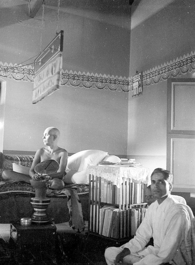 black-and-white photo of Sri Bhagavan seated on the couch in the Old Hall with Sub-Registrar Narayana Iyer seated in front