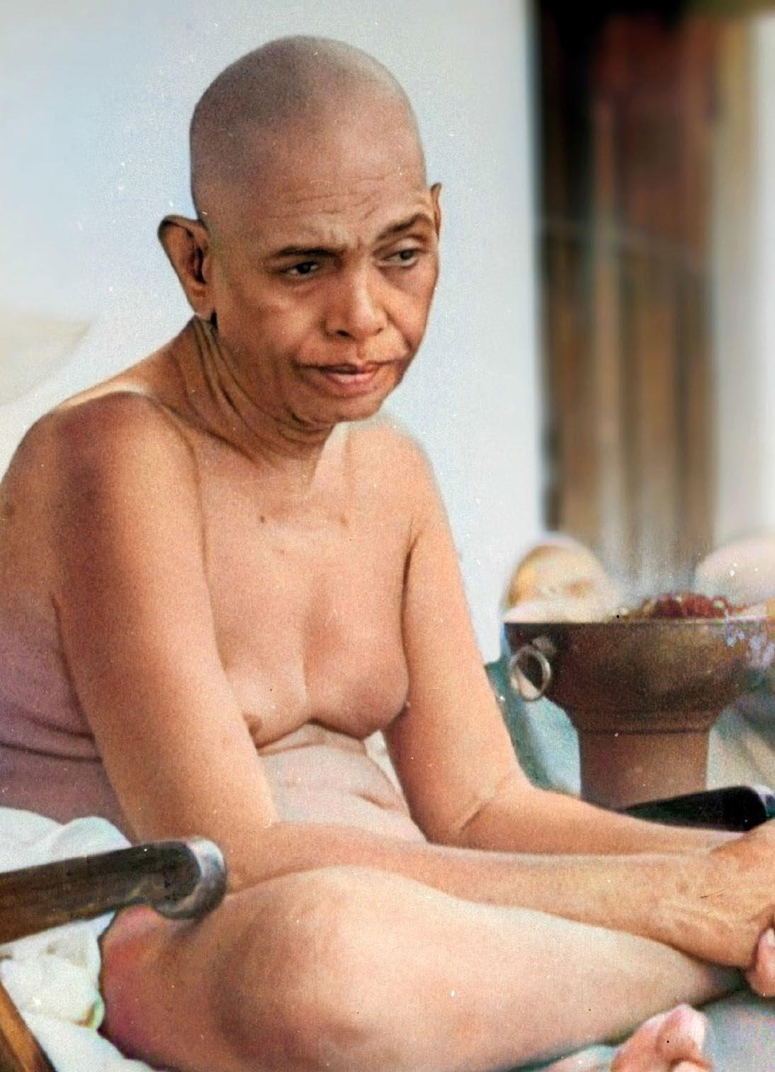 colour close-up photo of a shaven-headed man seated, a brass vessel at right