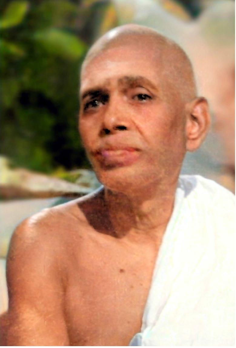 colour close-up photo of a shaven-headed man in a white cloth over one shoulder, foliage behind