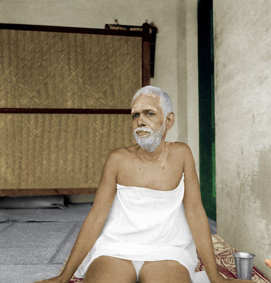 colour photo of Sri Bhagavan seated, wrapped in white cloth, before a woven-mat screen; no caption