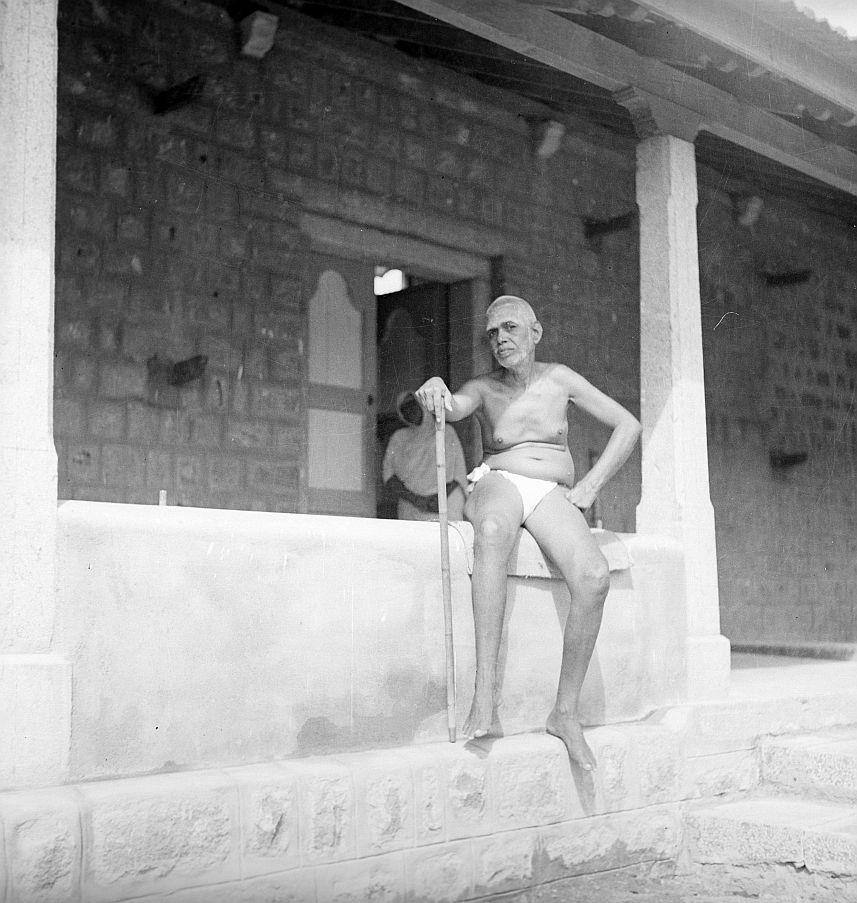 photo of Sri Bhagavan seated on a low wall by the kitchen building