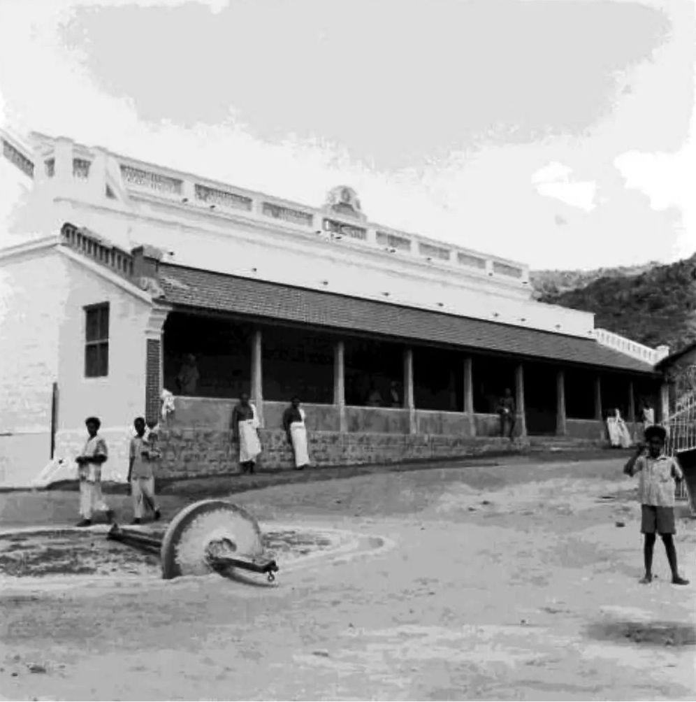 photo of the completed Dining Hall and Kitchen building with a grinding stone in the foreground
