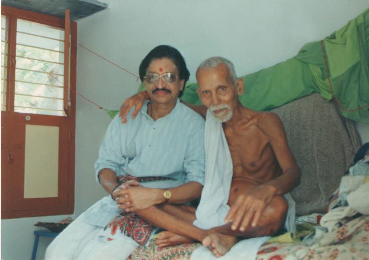 colour photo of a smiling man with his arm around the seated, elderly Annamalai Swami; no caption