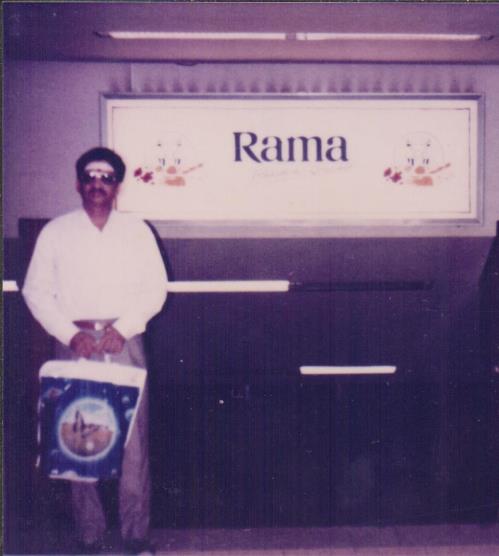 photo of Ganesan holding a bag standing before a sign reading Rama, Hamburg airport