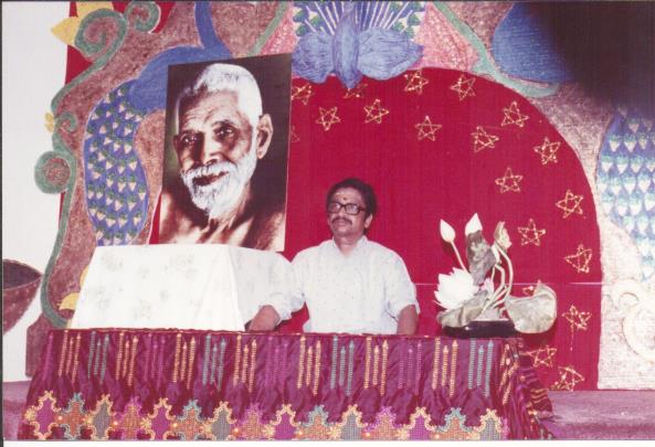 photo of Ganesan seated on a dais before a large portrait of Sri Bhagavan