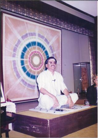 photo of Ganesan seated on a low stage before a large mandala backdrop