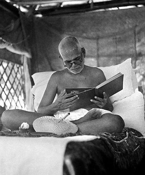 photo of Sri Bhagavan seated cross-legged on couch looking at a photo album, with palm-leaf fan