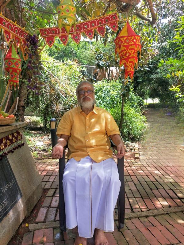 photo of V. Ganesan seated in a chair under a decorated canopy, in a garden