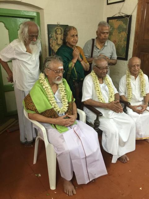 V. Ganesan garlanded and seated with two elderly men, others standing behind