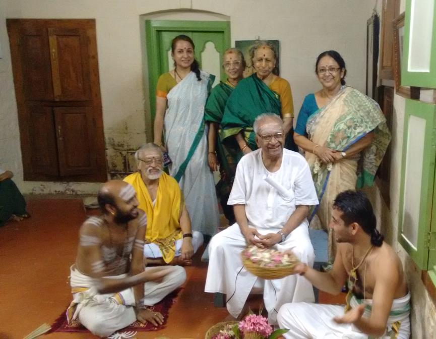 group of relatives seated and standing in a room with green door frames, priests in front