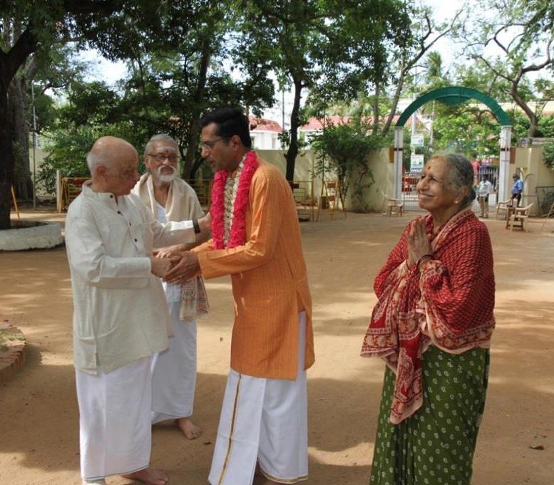 V. Ganesan and V. Subramanian greeting garlanded Dr. Anand outdoors, woman with folded hands