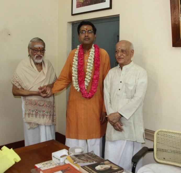 garlanded Dr. Anand standing between two elderly men in an office