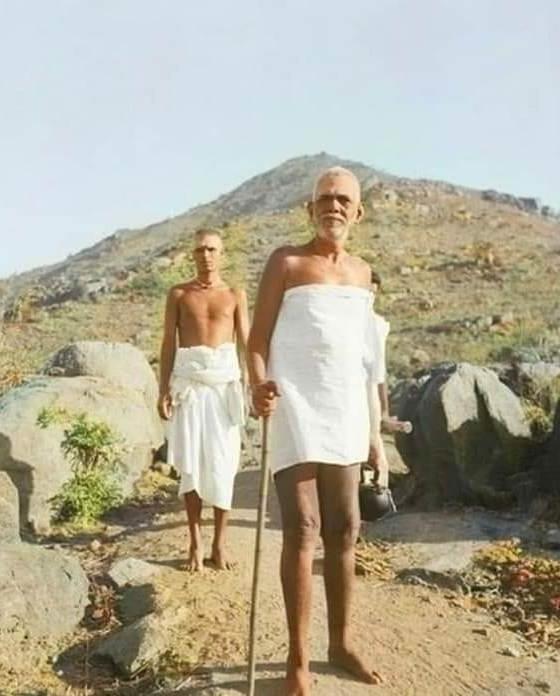photo of Sri Bhagavan standing with staff on the hill, an attendant behind him