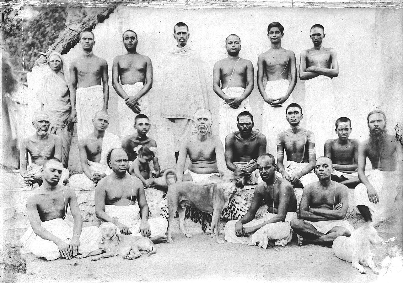 old group photograph of about twenty men and one woman, standing and seated in rows, with dogs and a leopard skin in front