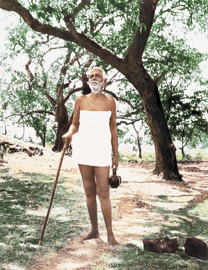 colour photograph of Sri Bhagavan standing under trees with a staff and kamandalu